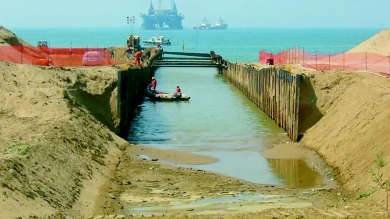 With the Castoro Sei pipe laying vessel in the background, the vital gas pipeline link is pulled ashore between the flanks of a cofferdam which crosses the sand dunes at Gela in Sicily.