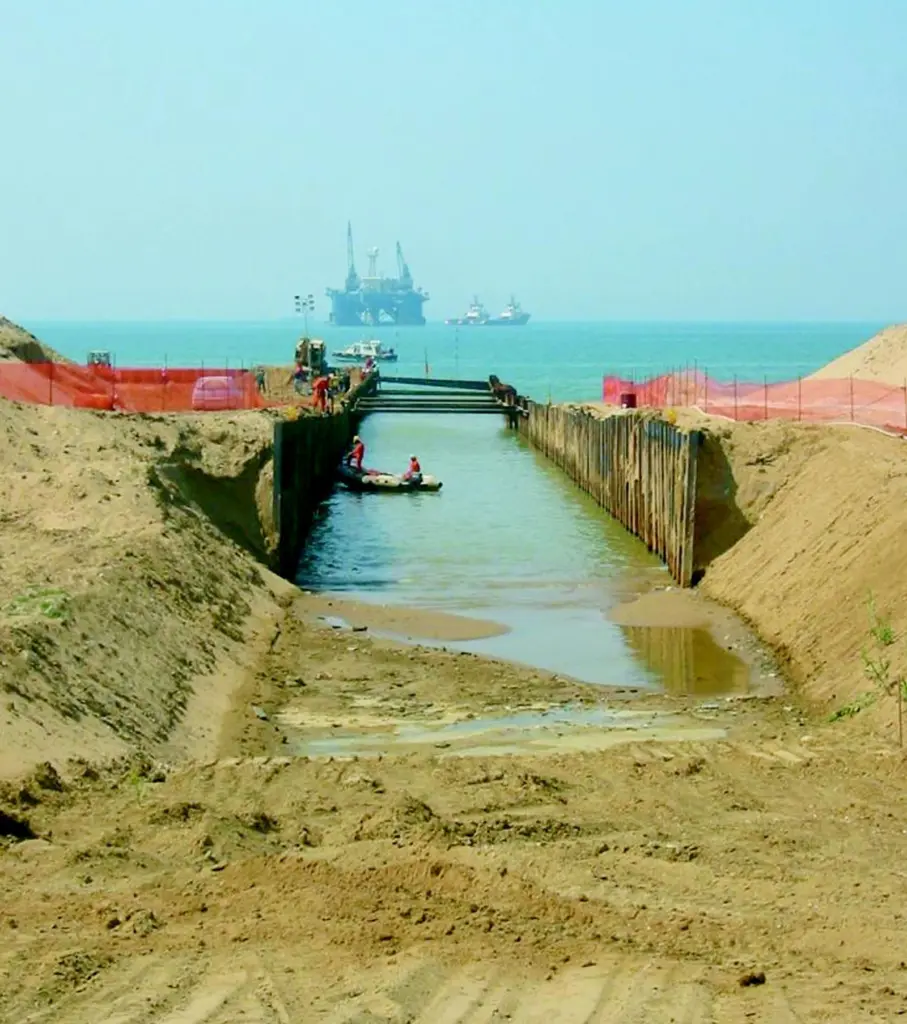 With the Castoro Sei pipe laying vessel in the background, the vital gas pipeline link is pulled ashore between the flanks of a cofferdam which crosses the sand dunes at Gela in Sicily.