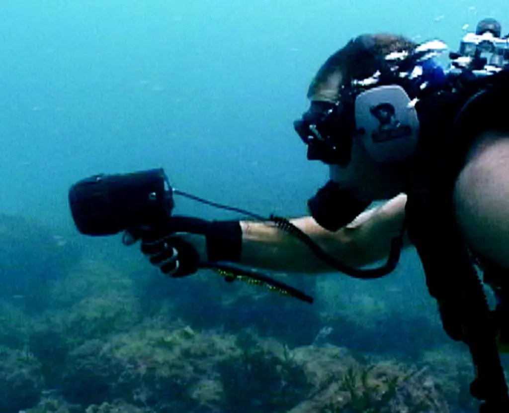 A diver with hand-held tracking device is directed towards the EMT pinger.