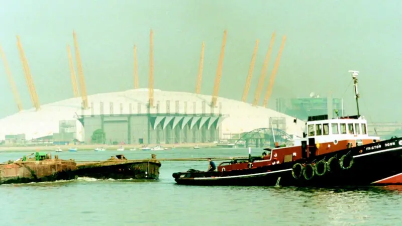 The GPS tug Friston Down tows a string of barges up river past the Millennium Dome.