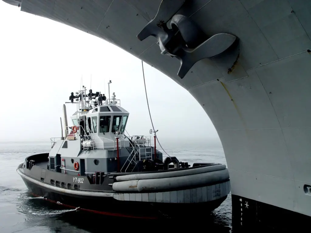 YTB Valiant’ is shown carrying out the work it was designed for under the bow of a major US warship.