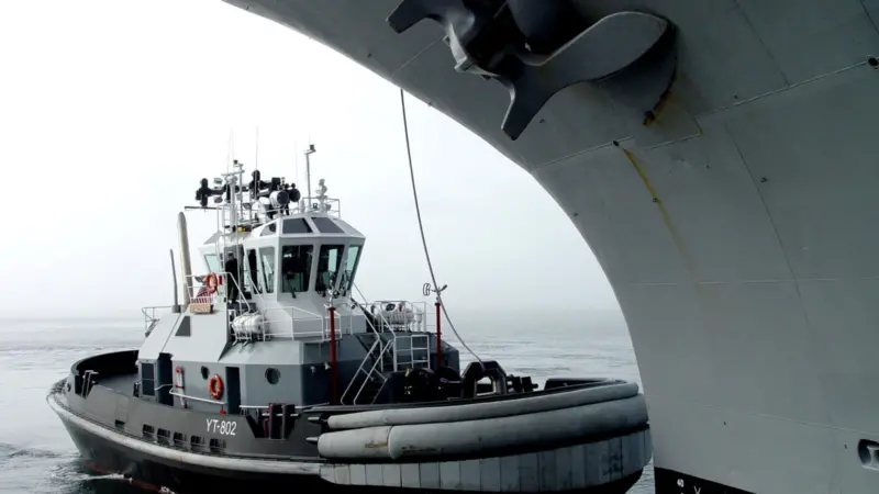 YTB Valiant’ is shown carrying out the work it was designed for under the bow of a major US warship.