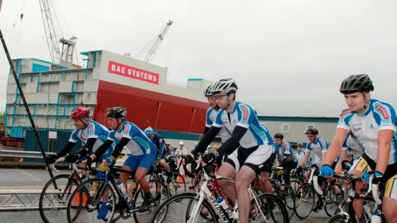 Charity ride cyclists leave BAE Systems’ Govan shipyard, with Lower Block 03 seen in the background.
