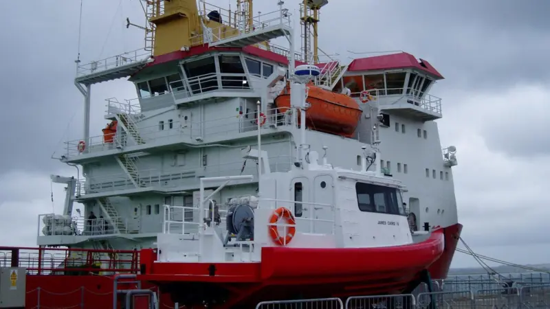 SMB James Caird IV is seen on the quay with mothership HMS Protector alongside.