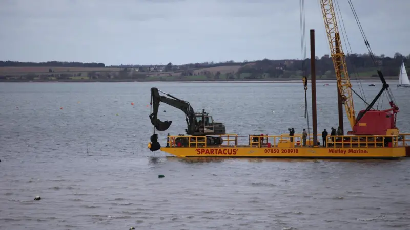 A bucket grab crane mounted on Mistley Marine's flat top barge Spartacus salvages the rocket remains.