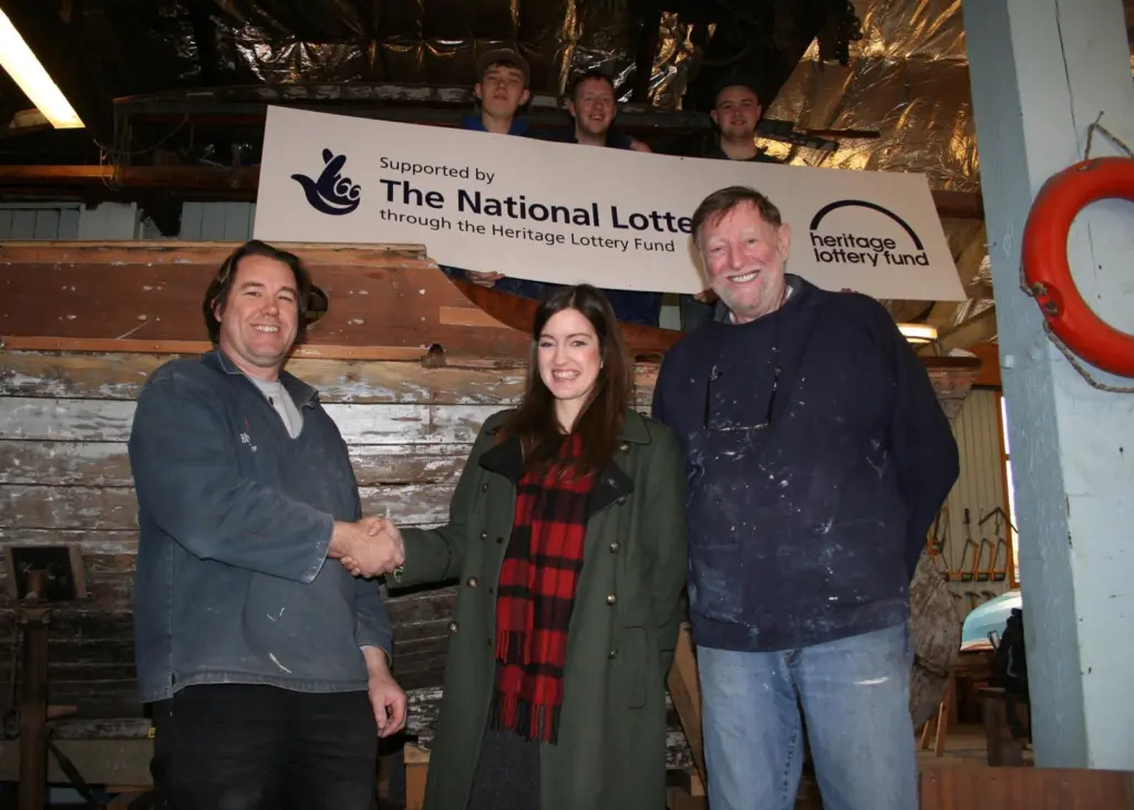 Jonny Bell (heritage boat builder with BTS) celebrates with Ellen Creighton (HLF) and volunteer Phil Charlton as trainees of the Blyth Tall Ship Project look on