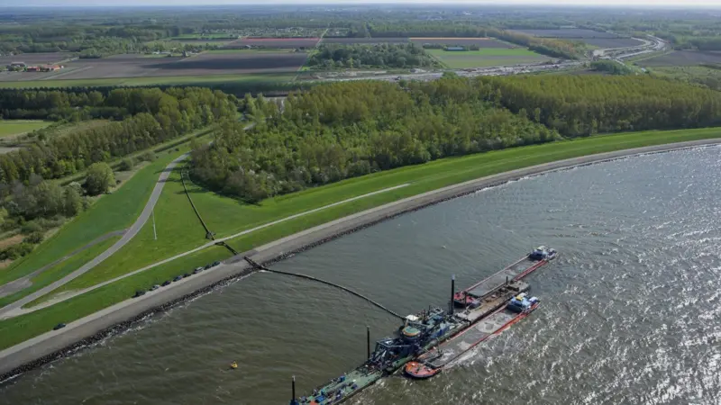 Supply barges provide sand which is pumped to the works site