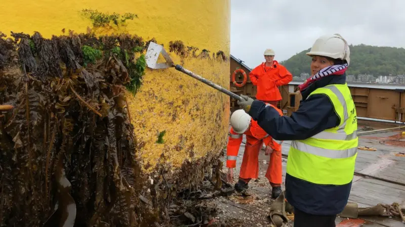 During the visit the Minister was given a tour of the buoy yard and had a go at some cleaning Photo: NLB