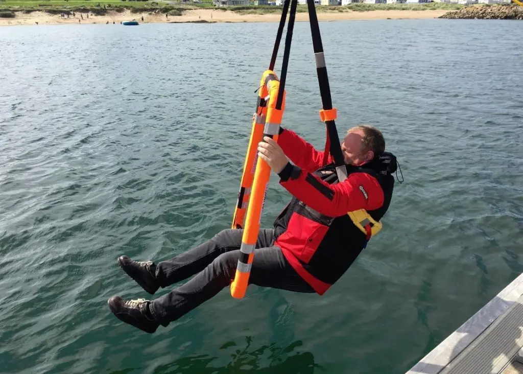 The casualty is captured by two slings, one a detachable chest sling and the other a leg sling formed by the floating frame