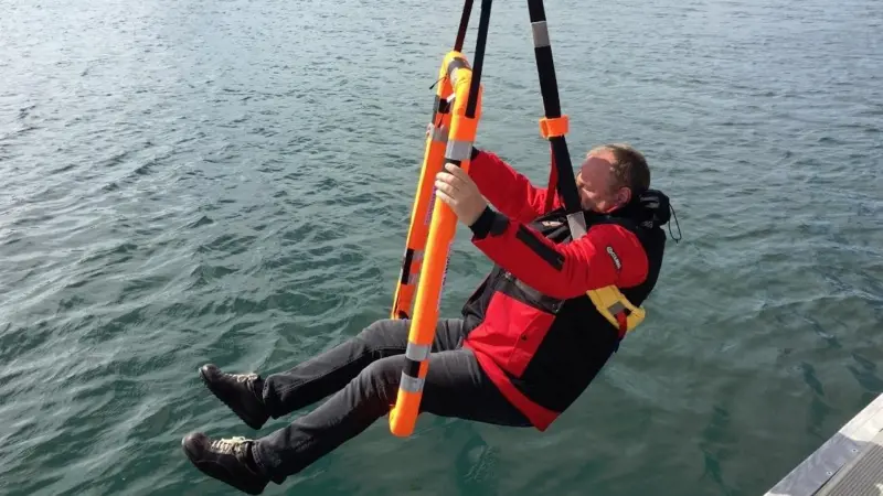 The casualty is captured by two slings, one a detachable chest sling and the other a leg sling formed by the floating frame