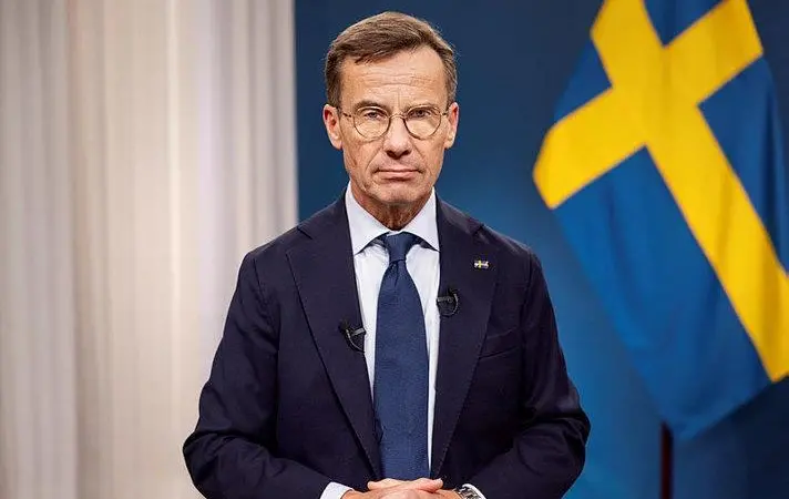 The image shows the the Swedish Prime Minister, Ulf Kristersson, pictured in front of a Swedish flag