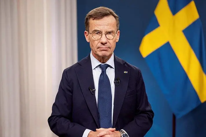 The image shows the the Swedish Prime Minister, Ulf Kristersson, pictured in front of a Swedish flag