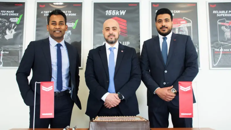 The image shows three men dressed in suits smiling at the camera