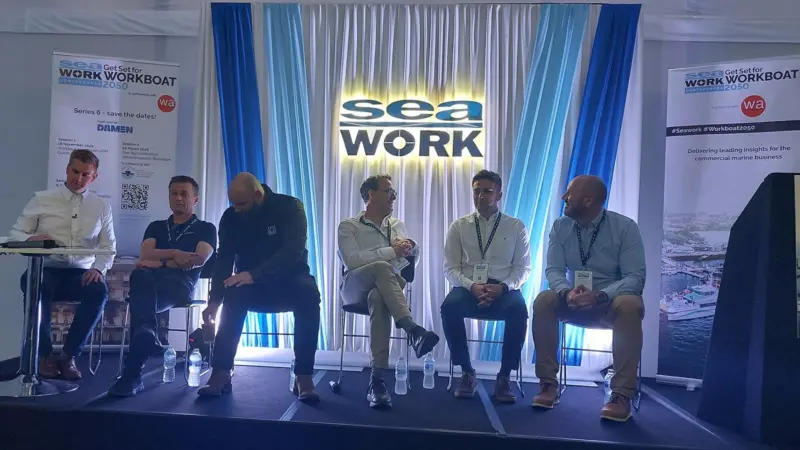 The image shows the speakers seated on stage