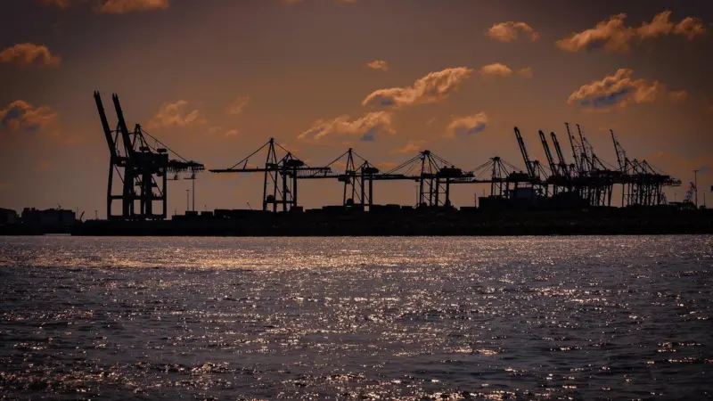 The image shows port cranes at sunset