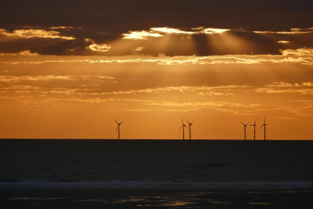The image shows a generic image of offshore wind turbines at sunset