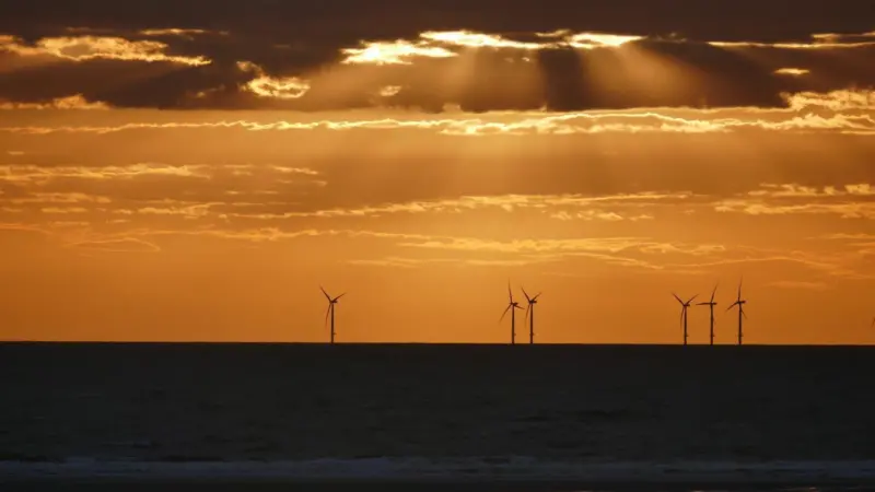 The image shows a generic image of offshore wind turbines at sunset