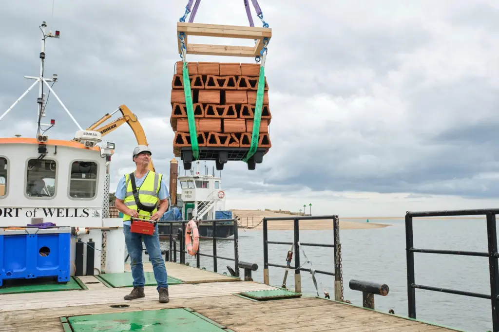 The image shows one of the clay bricks designed to house juvenile oysters being lowered into the water