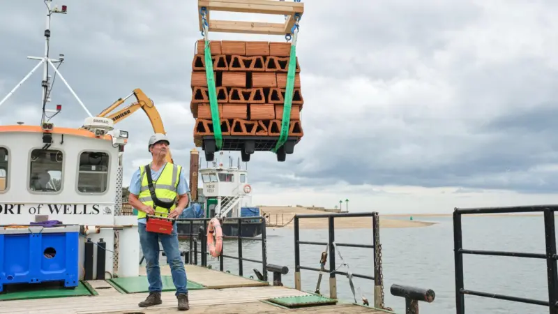 The image shows one of the clay bricks designed to house juvenile oysters being lowered into the water