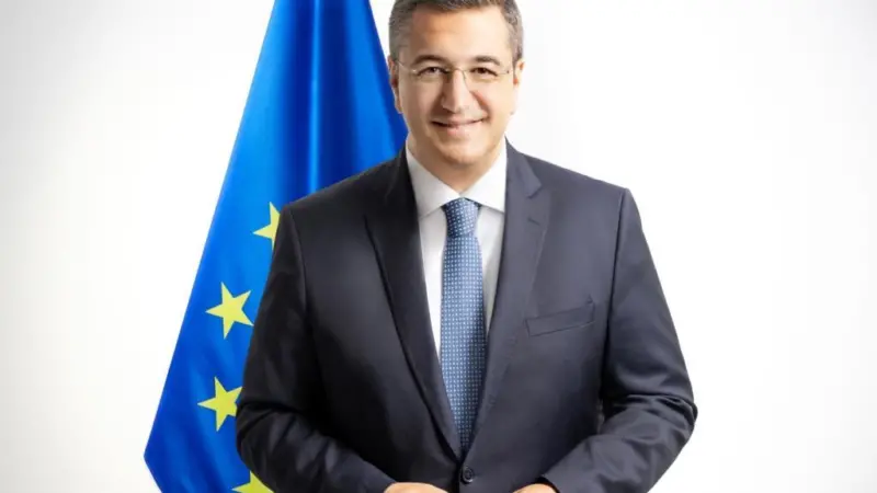 The image is of Commissioner Tzitzikostas standing in front of the EU flag
